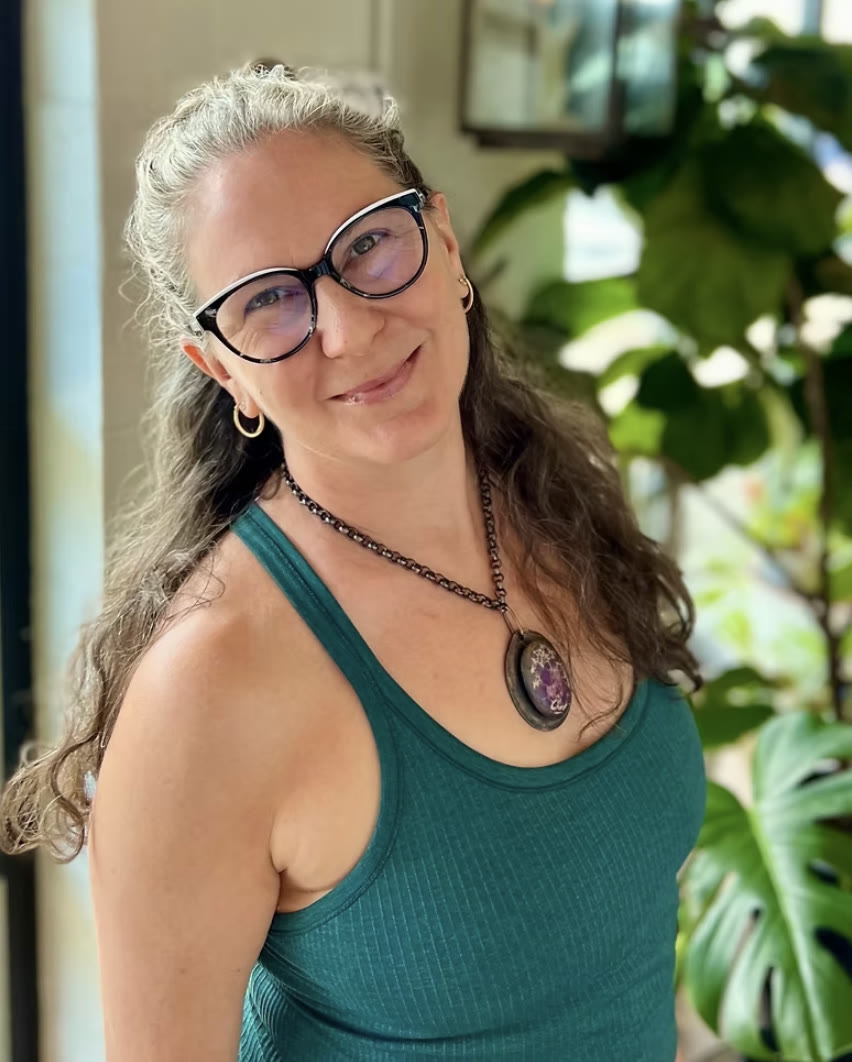Michelle smiling in a teal tank top, silver curls and a favorite pendant