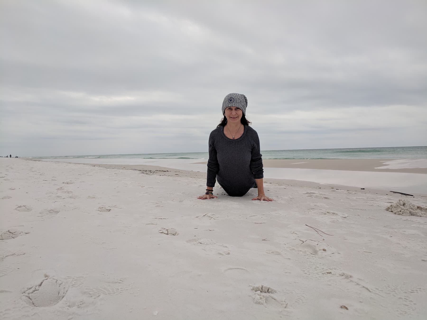 Michelle pressing up into a backbend on white sand, ocean behind her